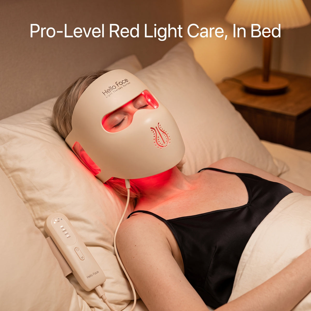 Blonde woman relaxing in bed wearing the 4D contoured LED face mask emitting gentle red light, connected to a handheld controller.