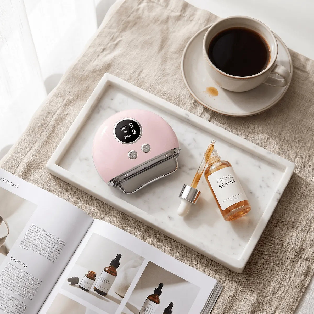 ELEVAURE EMS facial massager displayed with a bottle of facial serum and lifestyle elements on a marble tray.