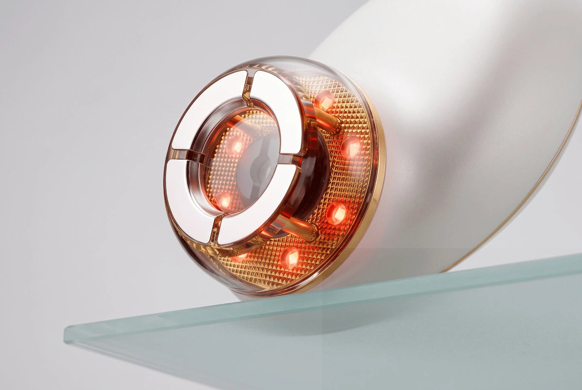 Close-up of the ELEVAURE facial device massage head emitting gentle red LED light therapy for collagen stimulation on a minimalist background.