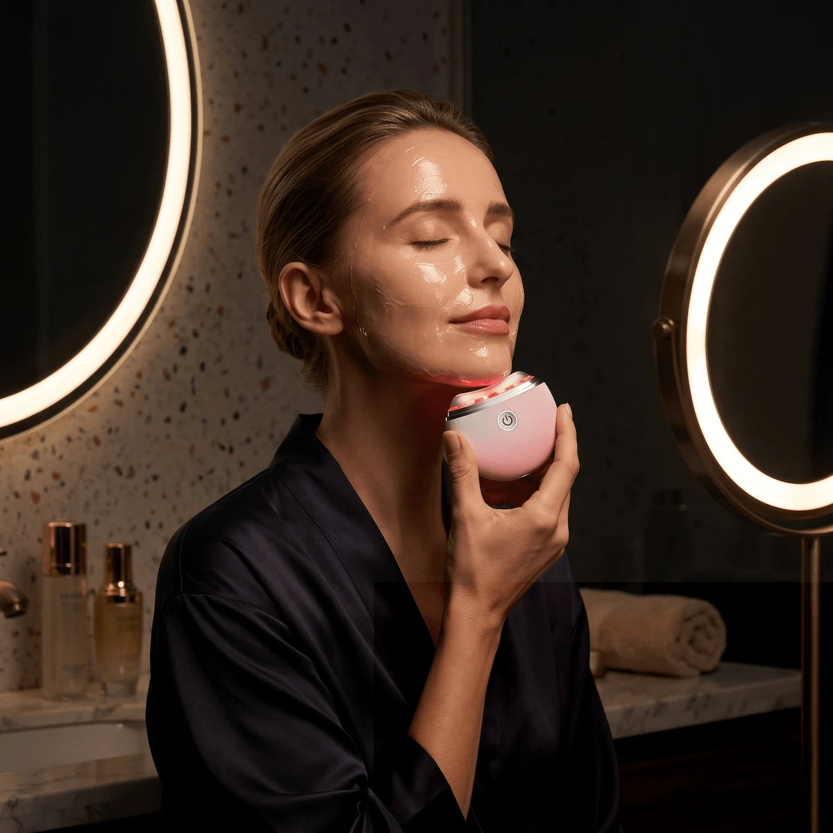 Elegant woman in her 40s using a microcurrent gua sha massager along her jawline as part of her evening anti-aging routine.