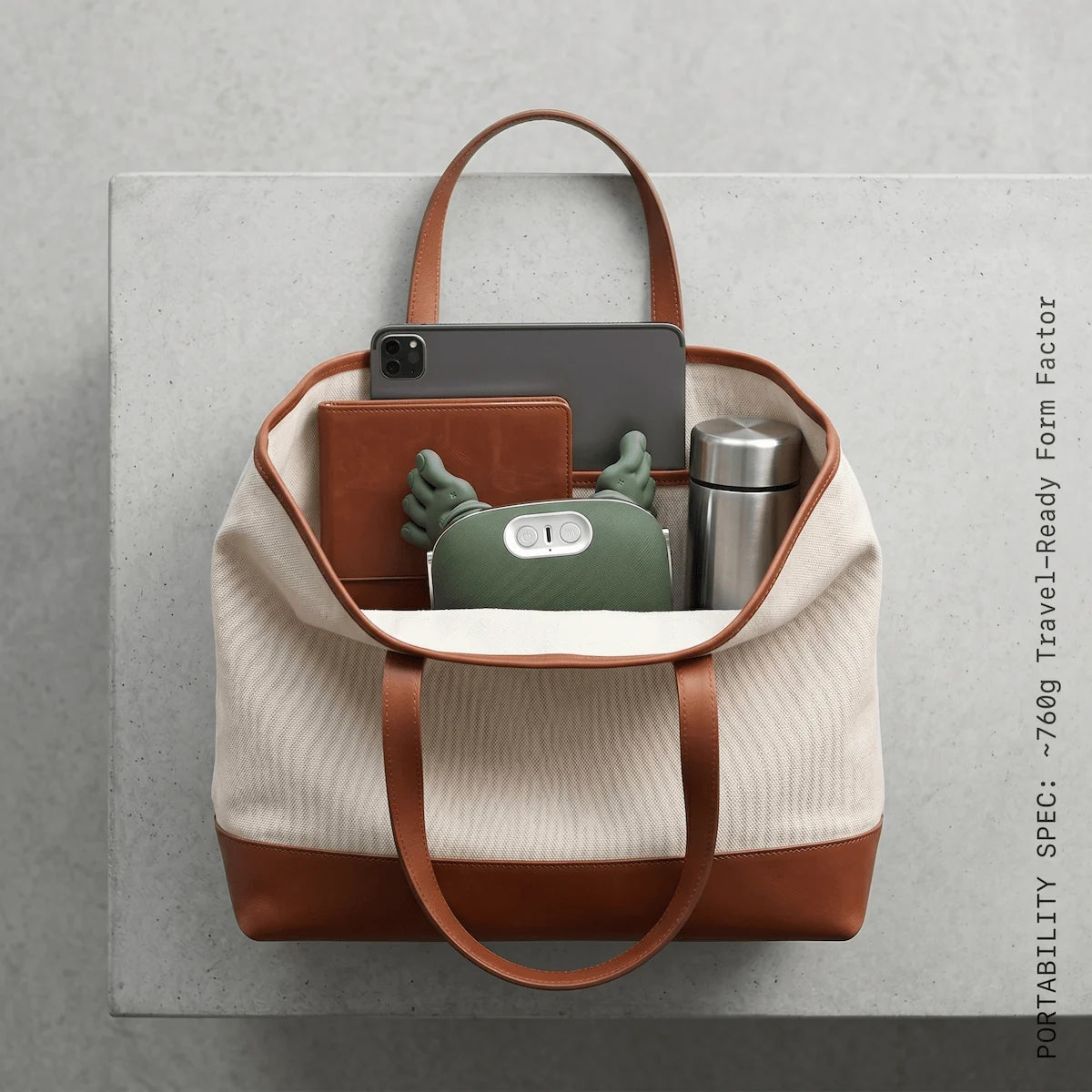 A lightweight sage green neck massager folded compactly inside a premium commuter tote bag next to standard tech accessories.