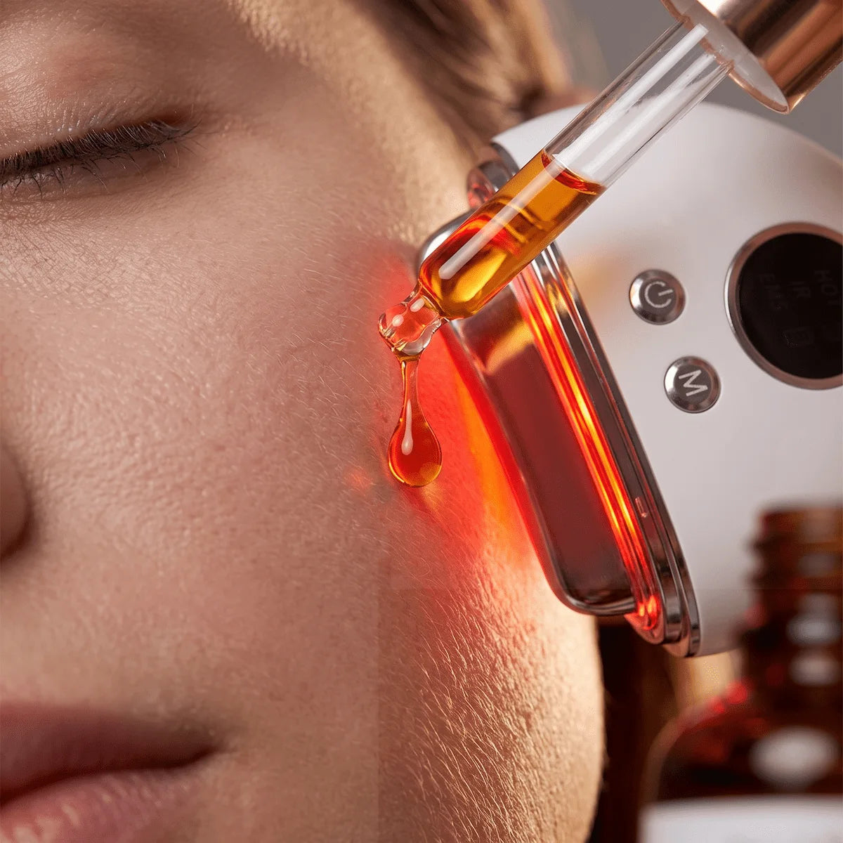 Close-up of a 4-in-1 EMS massager ready to massage a drop of facial serum into the skin.
