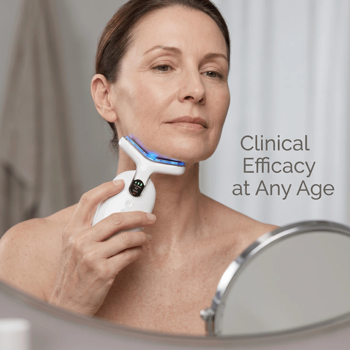 An elegant woman over 50 using an at-home EMS and RF facial sculpting device, showcasing real, unfiltered aging skin.
